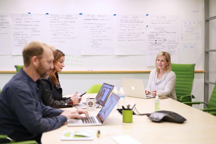 green conference room employees at table with laptops and whiteboard