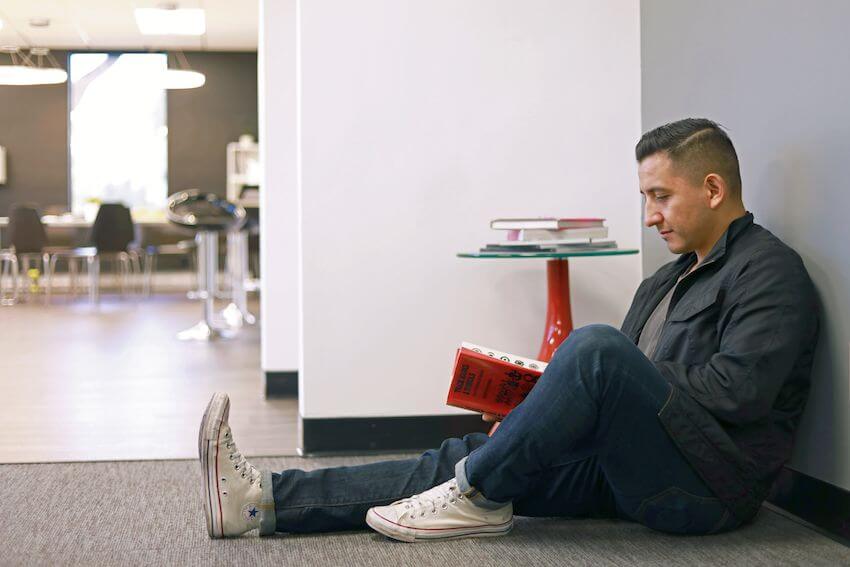 employee sitting against grey wall reading book